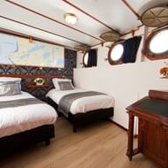 Tweepersoons hut aan boord van MS Princesse Royal met twee eenpersoonsbedden, gedessineerd hoofdeinde, patrijspoorten, houten bureau.