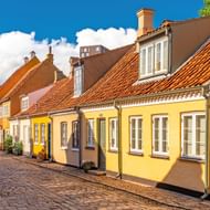 Rij traditionele Deense huizen met oranje pannendaken en gele gevels langs een kasseienstraat in Odense, Funen.