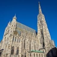 De Stefansdom in Wenen met zijn hoge gotische torenspits en kenmerkende gedecoreerde dak tegen een heldere blauwe lucht.
