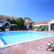 Groot rechthoekig zwembad bij Villa Matilde in Romano Canavese met bakstenen bestrating, houten ligstoelen, witte parasols en villagebouwen.