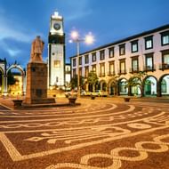 Avondzicht op het Portas da Cidade plein in Ponta Delgada, Azoren, met sierlijke klinkerbestrating, klokkentoren, boogpoorten en witte gebouwen.