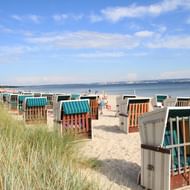 Rijen kleurrijke rieten strandkabines op zandstrand van Binz, Rügen. Duingras op voorgrond, Oostzee en blauwe hemel met wolken op achtergrond.