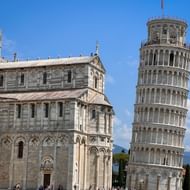 De Scheve Toren van Pisa en de Kathedraal van Pisa met witte marmeren gevels onder blauwe hemel. De iconische hellende klokkentoren staat prominent naast de kathedraal.
