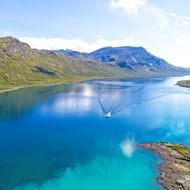 Luchtfoto van een diepblauw bergmeer bij Bitihorn in Nationaal Park Jotunheimen, omringd door groene heuvels en rotsachtige bergen onder bewolkte lucht.