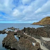 Natuurlijke zwembaden in Porto Moniz gevormd door vulkanisch gesteente met helder turquoise water, witte looppaden en oceaanzicht.