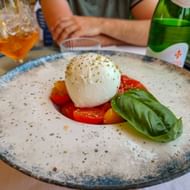 Caprese salade met burrata, gesneden tomaten en verse basilicum op een gespikkeld bord in Bardolino, Gardameer. Drankjes op de achtergrond.