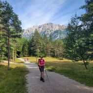 Wandelaar met roze rugzak en wandelstokken op bospad bij Ferchenseehöhe met Zugspitze bergmassief op de achtergrond onder blauwe lucht.