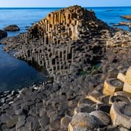 Zeshoekige basaltzuilen bij Giant's Causeway die zich uitstrekken in de kalme blauwe zee onder heldere hemel in County Antrim, Noord-Ierland.