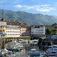 Jachthaven vol witte boten in Asturische kustplaats, met kleurrijke gebouwen met traditionele galerijen en groene bergen op achtergrond.