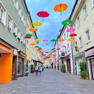 Voetgangersstraat in oude stad Villach met kleurrijke paraplu's boven de straat. Veelkleurige gebouwen met winkels aan beide zijden.