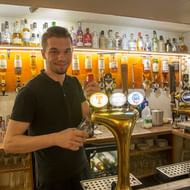 Barkeeper in Inveroran pub in Schotland Glimlachende barkeeper in groen poloshirt achter de bar in Inveroran pub, met biertaps, flessen en whisky-dispensers zichtbaar.