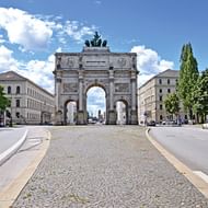 De Siegestor triomfboog in München met drie bogen, sierlijke reliëfs en bronzen quadriga bovenop. Kasseienstraat leidt naar de boog.