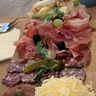 Houten plank met Sloveense vleeswaren, prosciutto, salami, geraspte kaas, olijven, augurken en verse kruiden op bruin papier.