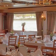 Elegante eetzaal op MS Switzerland met gedekte tafels, houten stoelen, witte tafelkleden en grote ramen met uitzicht op de rivier.