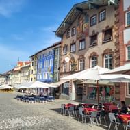 Geplaveide voetgangerszone in Bad Tölz met kleurrijke historische gebouwen, café-terrassen en witte parasols onder blauwe lucht.