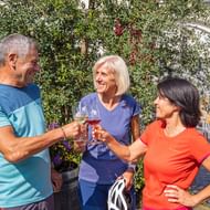 Drie fietsers proosten met wijnglazen in een zonnige binnenplaats in Forst aan de Duitse Wijnroute, omringd door groen en bloemen.