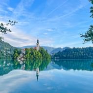 Kerk met klokkentoren op klein bebost eiland in het Meer van Bled, Slovenië. Perfecte reflectie in kalm water, omringd door bergen.