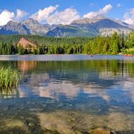 Helder bergmeer weerkaatst wolken en lucht in de Hoge Tatra. Een hotel staat tussen dichte bossen met dramatische pieken op de achtergrond.