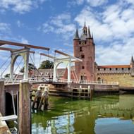 Oude haven van Zierikzee met witte ophaalbrug over groen water, rode bakstenen kerktoren met spits op achtergrond onder blauwe lucht.