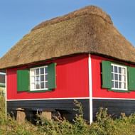 Rood en blauw houten huis met dik rieten dak en groene luiken op Funen eiland, Denemarken. Het huis staat op palen bij de kust.