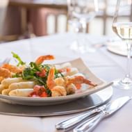 Witte asperges met garnalen, kruiden en blokjes groenten op wit bord, geserveerd met wijnglazen op elegante restauranttafel.