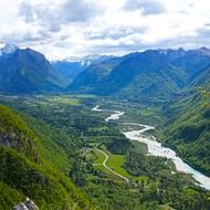 Panoramisch uitzicht op de turquoise Soča rivier die door de groene Bovec vallei in Slovenië kronkelt, omringd door besneeuwde bergen.