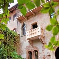 Stenen balkon van Romeo en Julia in Verona met sierlijke balustrade, omlijst door groene wijnbladeren. Middeleeuwse bakstenen gevel zichtbaar.