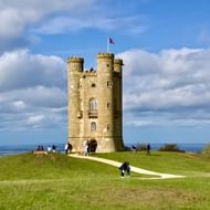 Broadway Tower in Cotswolds landschap Broadway Tower, een hoge stenen kasteel toren met Britse vlag, staat op een groene heuvel met bezoekers op de paden.