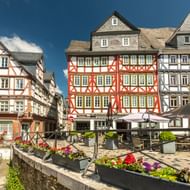 Historisch Kornmarkt plein in Wetzlar met kleurrijke vakwerkhuizen, buitenterrassen en bloembakken onder blauwe hemel.