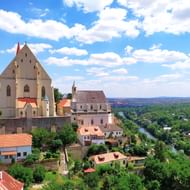 Kasteelcomplex Znojmo in Moravië, Tsjechië, met witte kerk en vestingmuren boven een rivierdal met groene bossen.