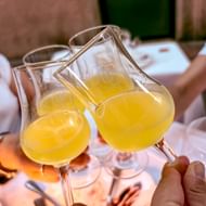 Drie glazen gele limoncello klinken boven een gedekte tafel met borden en bestek.