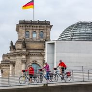 Groep fietsers met fietsen op moderne brug bij Berlijn Reichstag gebouw met Duitse vlag en glazen koepel op Spree fietsroute.