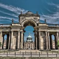 Neues Palais in Potsdam met een grote barokke zuilengalerij met Korinthische zuilen, sierlijke sculpturen en een centrale boogvormige ingang onder blauwe hemel.