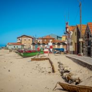 Kleurrijke vissersboten op zandstrand in Vila Chã met traditionele vissershuizen met oranje pannendaken onder blauwe lucht.