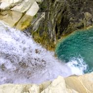 Water stroomt over met mos bedekte rotsen in een turquoise poel in Hidden Valley, Albanië. Wit schuim spat tegen beige kalksteenrotsen.