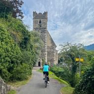 Fietser in turquoise shirt rijdt naar een stenen kerk met toren in Sankt Michael, Wachau. Gele bewegwijzering langs het pad zichtbaar.