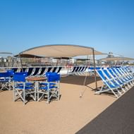 Zonnedek van MS Lisabelle met blauw-wit gestreepte ligstoelen, blauwe klapstoelen en beige zonnezeilen onder heldere hemel.