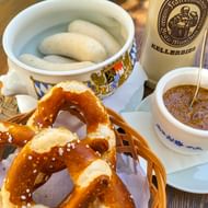 Traditionele Beierse maaltijd met gezouten pretzels in rieten mand, witte worsten in decoratieve kom, mosterd en Kellerbier fles.