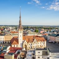 Luchtfoto van het stadsplein van Olomouc met wit stadhuis en hoge klokkentoren. Historische gebouwen met rode daken rondom het plein.