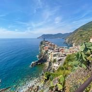Dorp Manarola op rotsachtige kliffen boven de turquoise Ligurische Zee, met kleurrijke huizen en groene hellingen onder blauwe lucht.