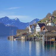 Schilderachtig uitzicht op Walensee met traditionele Zwitserse huizen langs de oever, houten pier in kalm blauw water en besneeuwde Alpen.