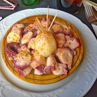 Traditionele Spaanse pulpo geserveerd op wit keramisch bord met gesneden octopustentakels, gekookte aardappel en paprika.