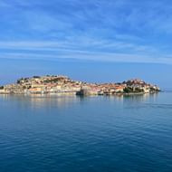 Kustgezicht van eiland Elba met kleurrijke mediterrane gebouwen aan het water onder een blauwe hemel met witte wolken.