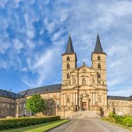 Klooster Michelsberg in Bamberg met romaanse tweeling-torenkerk en barokke gebouwen onder blauwe bewolkte hemel.