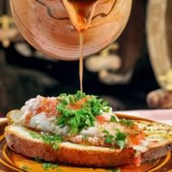 Caldo de peixe wordt uit een aarden pot geschept over brood met witte vis en verse kruiden op een bruin bord op de Azoren.