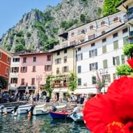 Pittoreske haven van Limone sul Garda met kleurrijke boten afgemeerd in helder water, omringd door traditionele Italiaanse gebouwen.