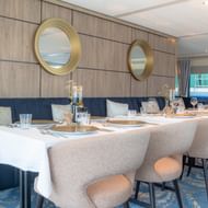 Modern restaurant interieur op MS Lisabelle met beige gestoffeerde stoelen, witte tafellakens en houten wandpanelen met ronde gouden spiegels.