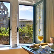 Ontbijttafel met wijn en eten bij open ramen met glas-in-lood. Uitzicht op stenen kerktoren en tuin in Castilië, Spanje.