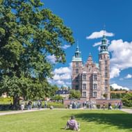 Historisch kasteel Rosenborg met kenmerkende groene koperen torens en rode bakstenen gevel, omgeven door weelderig groen parklandschap.