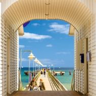 Zicht door de gewelfde ingang van het Ostseebad Göhren piergebouw, met houten pier die de Oostzee in loopt met witte lantaarnpalen en bezoekers.